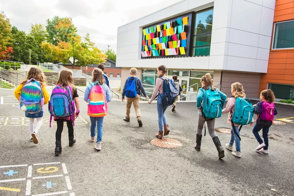 Group of children with backpacks walking toward colorful modern school building.